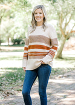 Blonde model wearing cream sweater with brown and rust stripes with jeans.