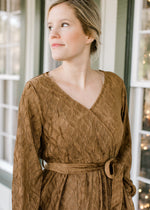 NEck detail of Blonde model in textured warm brown faux wrap dress.