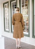BAck view of Blonde model in textured warm brown faux wrap dress.