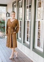 Blonde model in textured warm brown faux wrap dress and heels on porch.