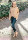 Blonde model wearing a taupe long sleeve top with jeans with mules. 