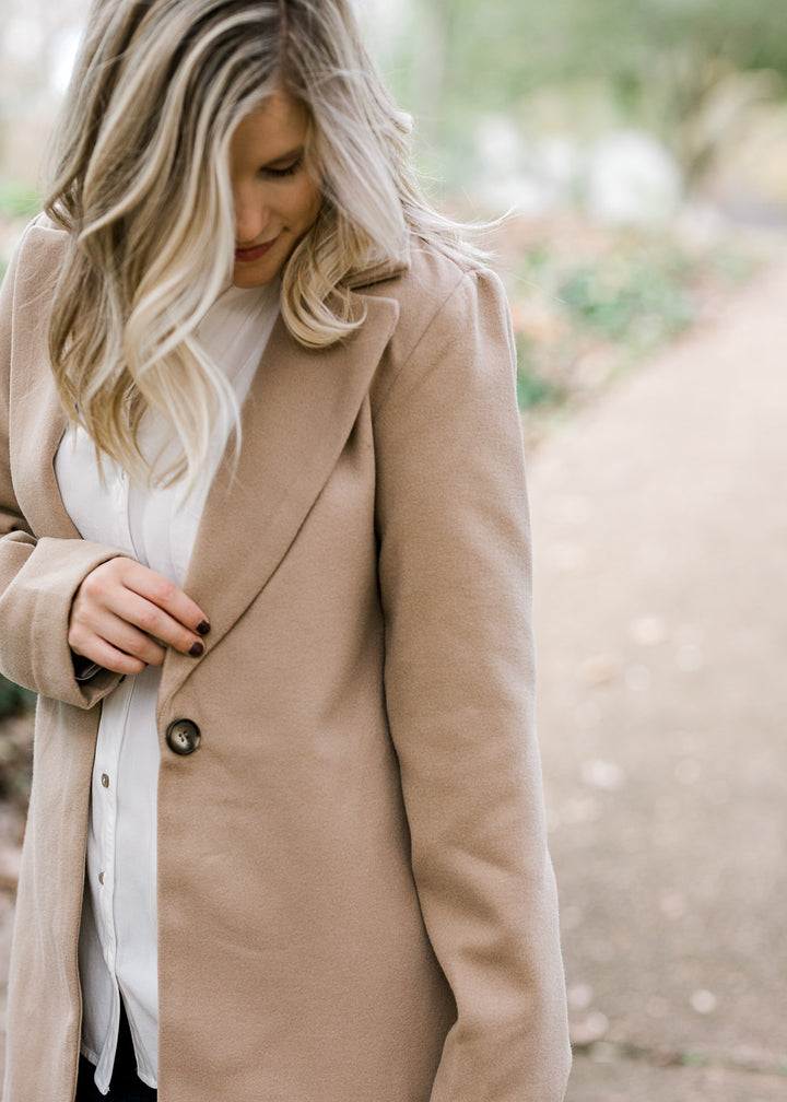 View of single button closure on camel colored coat.