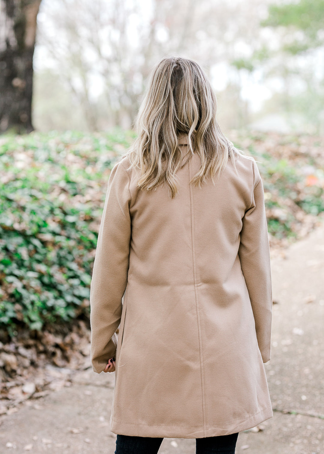 Back view of Blonde model wearing camel color coat. 