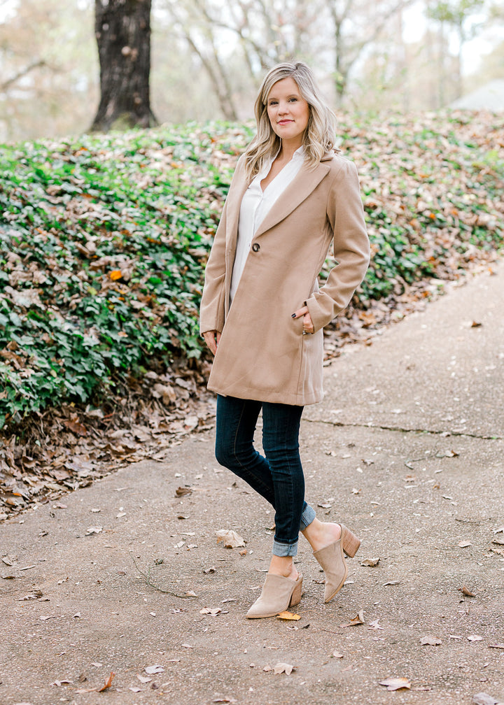 Blonde model wearing camel color coat with white top and jeans.