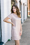 Brunette model wearing short sleeve, champagne colored, sequin dress.