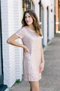 Brunette model wearing short sleeve, champagne colored, sequin dress.