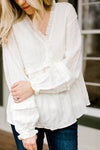 Blonde model wearing a cream top with ruffles details.