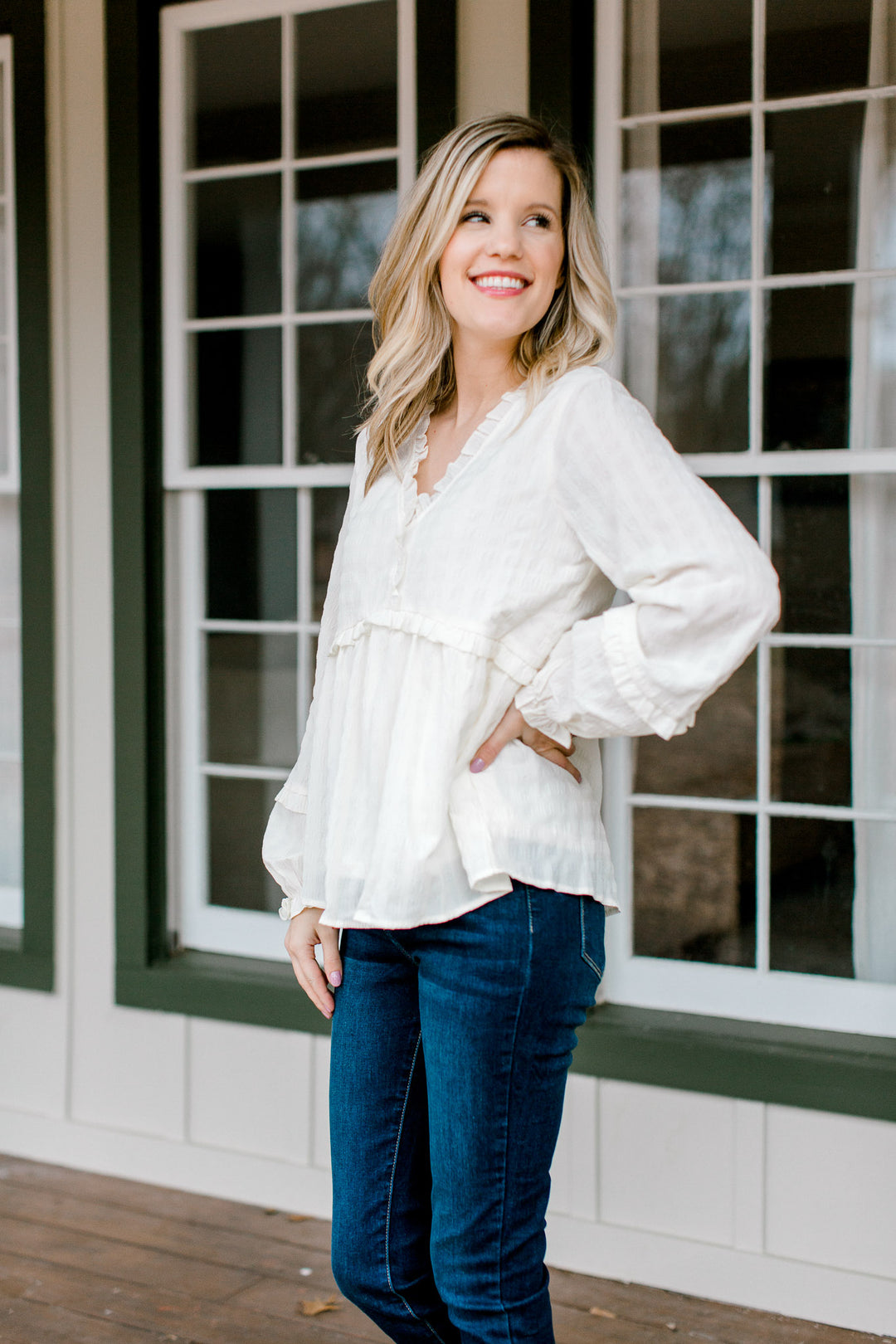 Blonde model wearing a cream long sleeve top with ruffles details.