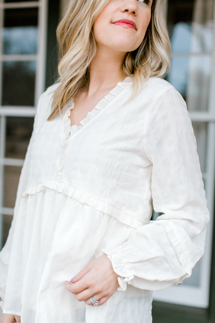 Close up view of a cream top with textured material on a Blonde model. 