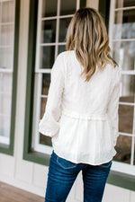 Back view of Blonde model wearing a cream top with a textured material.