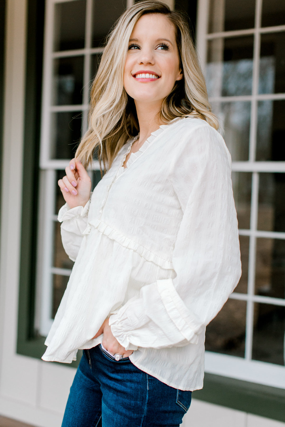 Blonde model wearing a v-neck,cream top with ruffles details.
