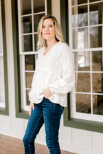 Blonde model wearing a cream top with ruffles details with jeans.