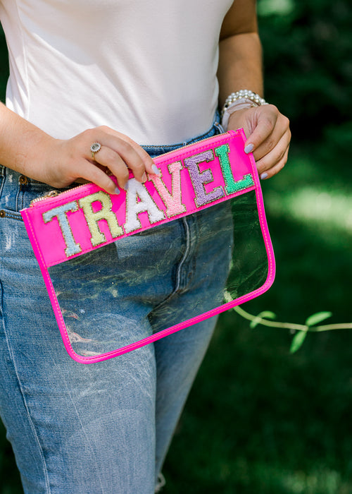 Model holding clear pouch with Travel on top in hot pink. 