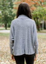 Back view of brunette model wearing light blue sweater with cowl neck.