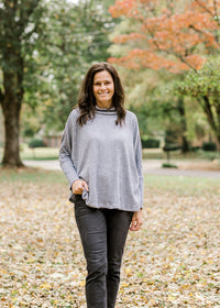 Brunette model wearing black jeans and light blue sweater with cowl neck.  