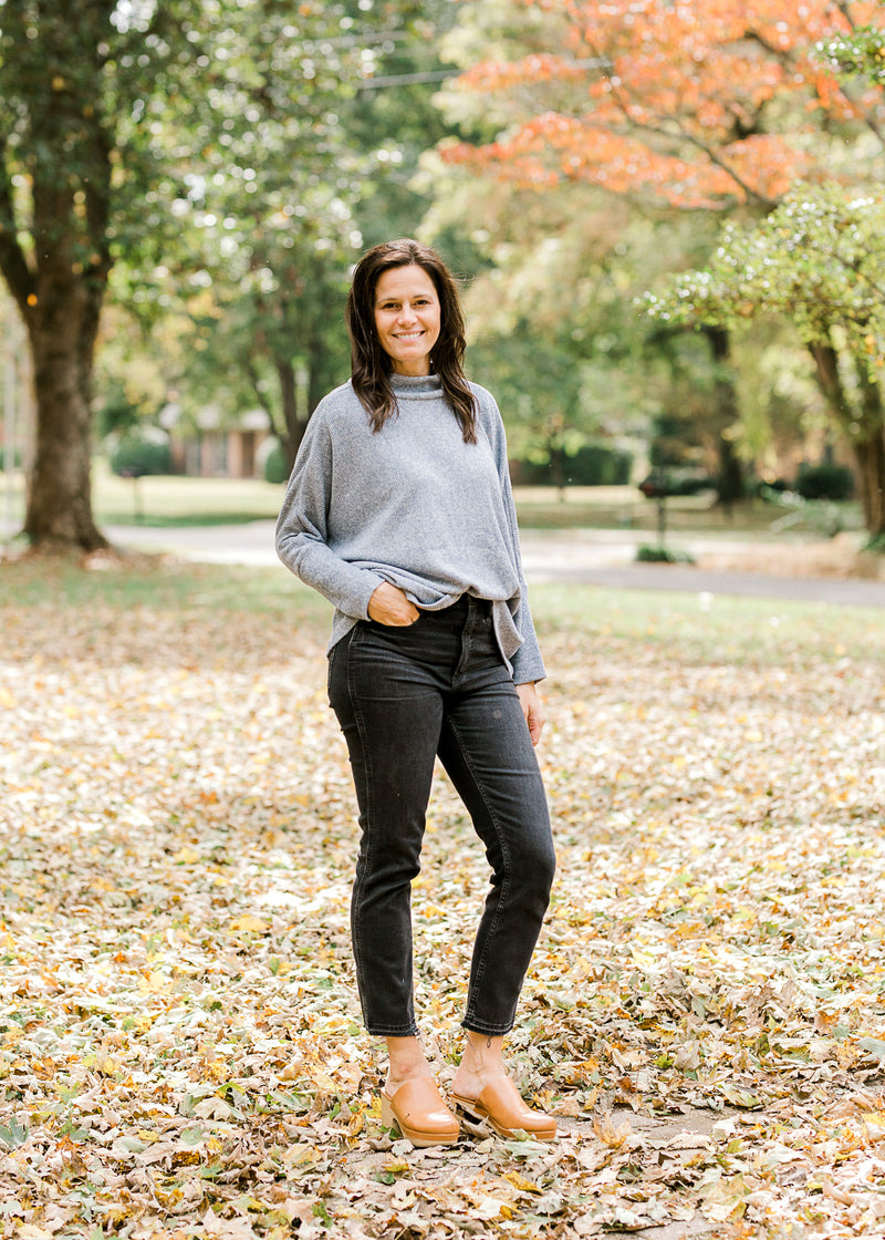 Brunette model wearing light blue sweater with black jeans and heeled mules.