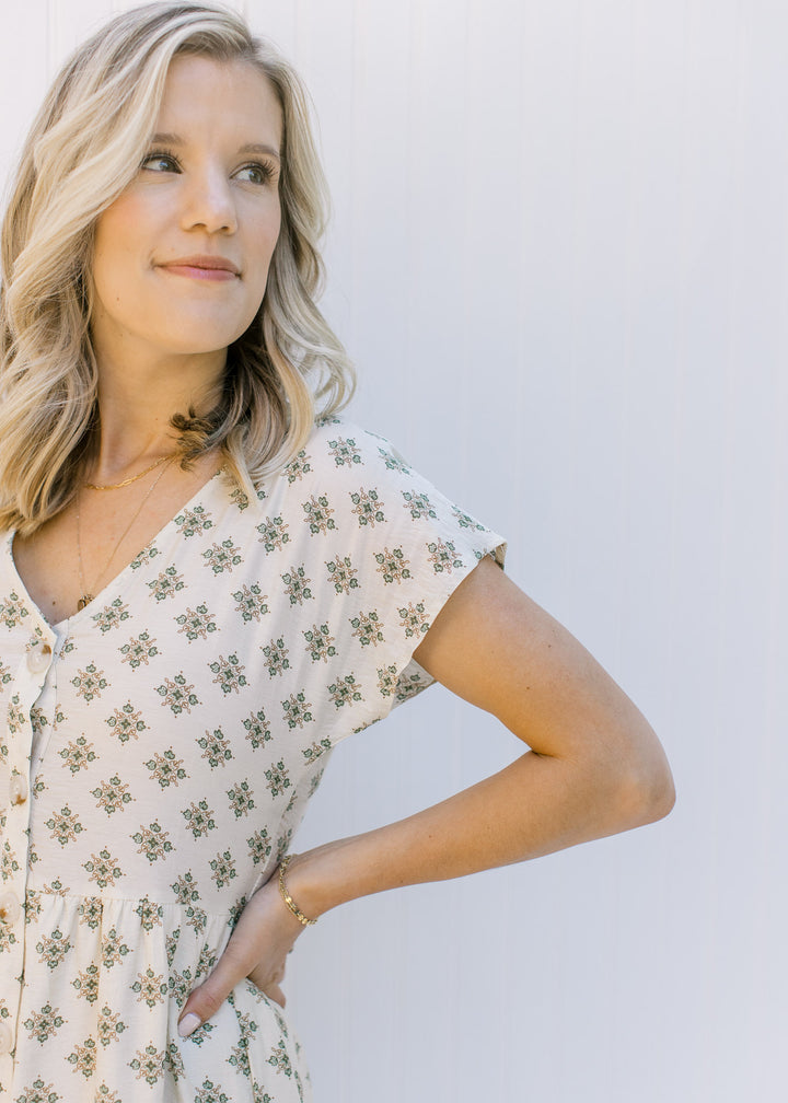 Close up view of buttons on a model wearing a cream dress with a hunter green pattern. 