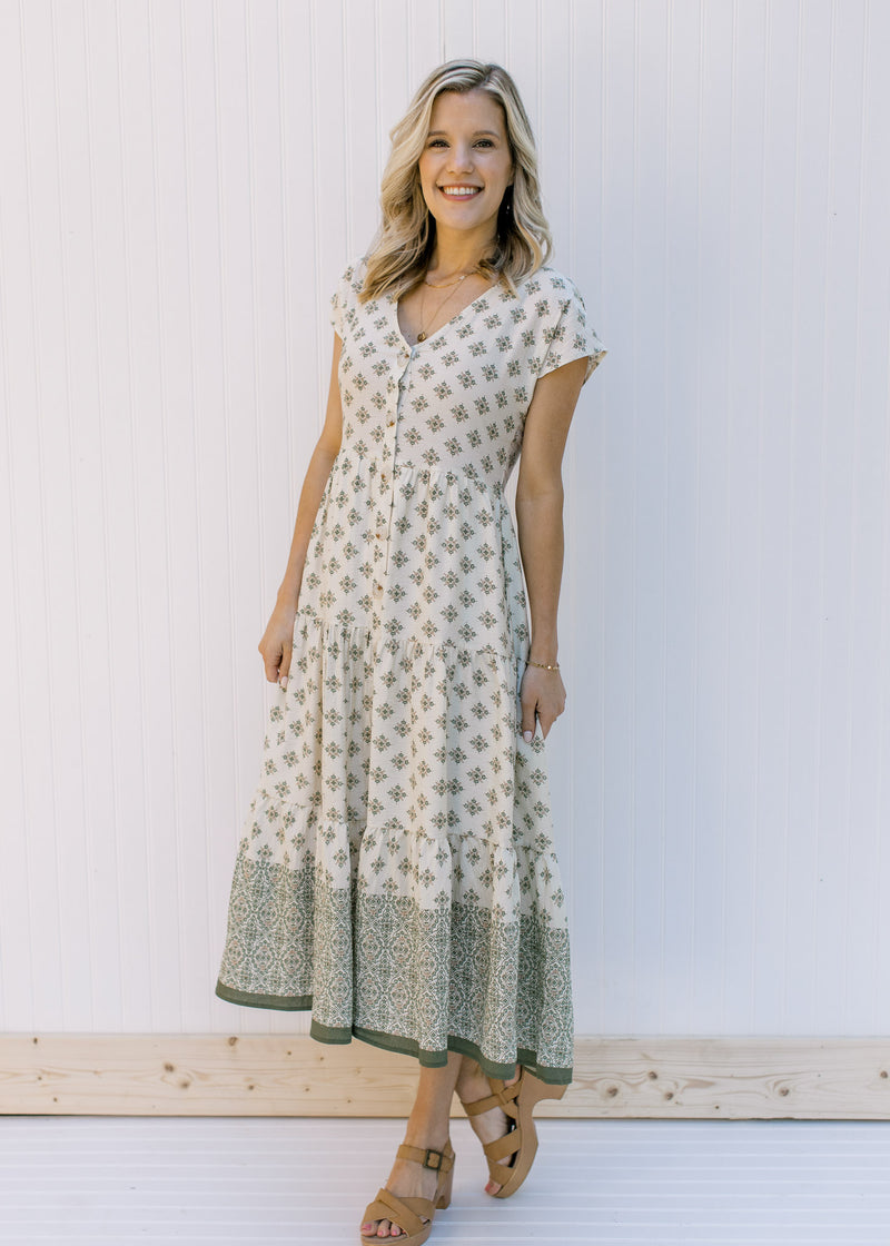 Model wearing a cream, midi dress with hunter green pattern and short sleeves and sandals. 