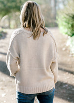 Back view of Blonde model wearing cream cable knit sweater.