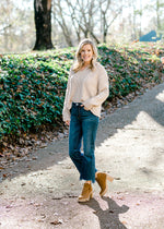 Blonde model wearing cream cable knit sweater with jeans and booties.