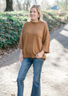 Blonde model wearing copper colored sweater with cuffed 3/4 sleeves. 