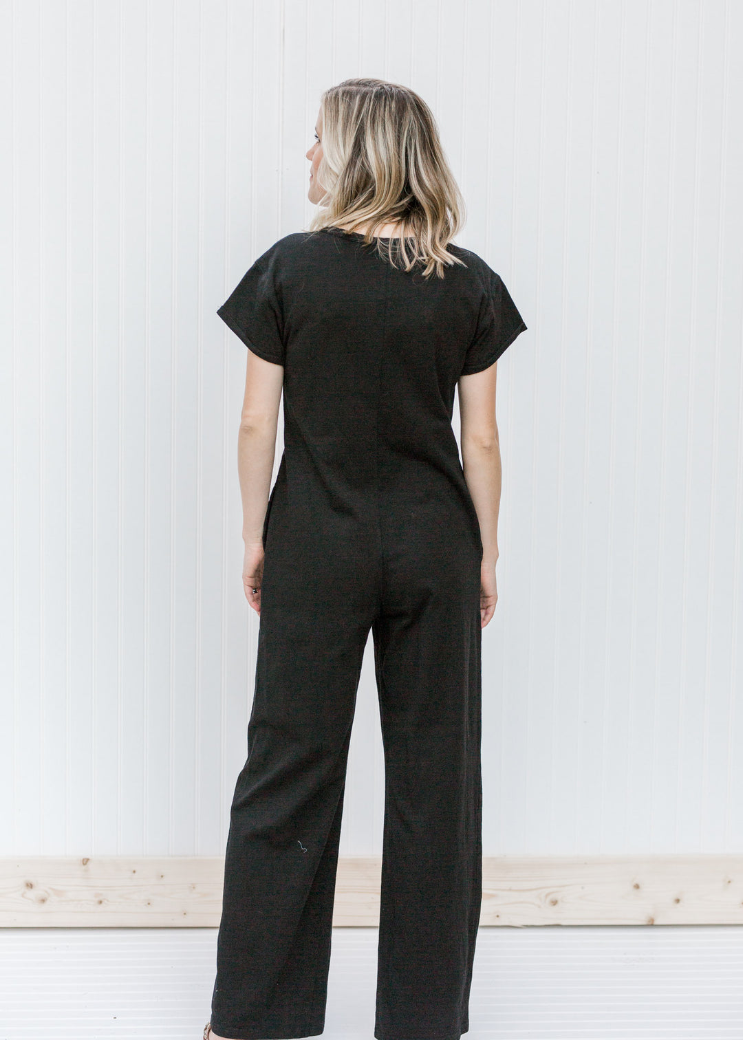 Back view of Blonde model wearing a black jumpsuit.