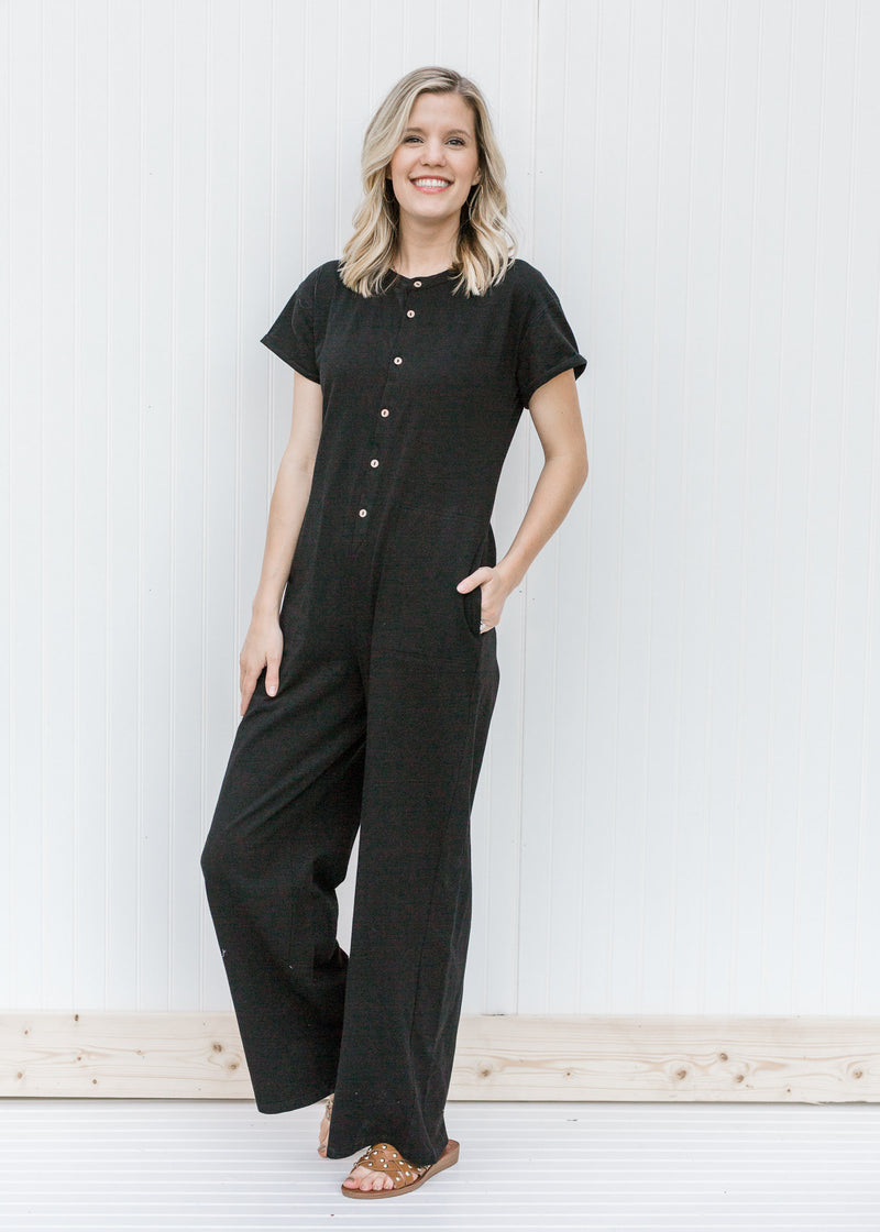 Blonde model wearing a black jumpsuit with sandals. 