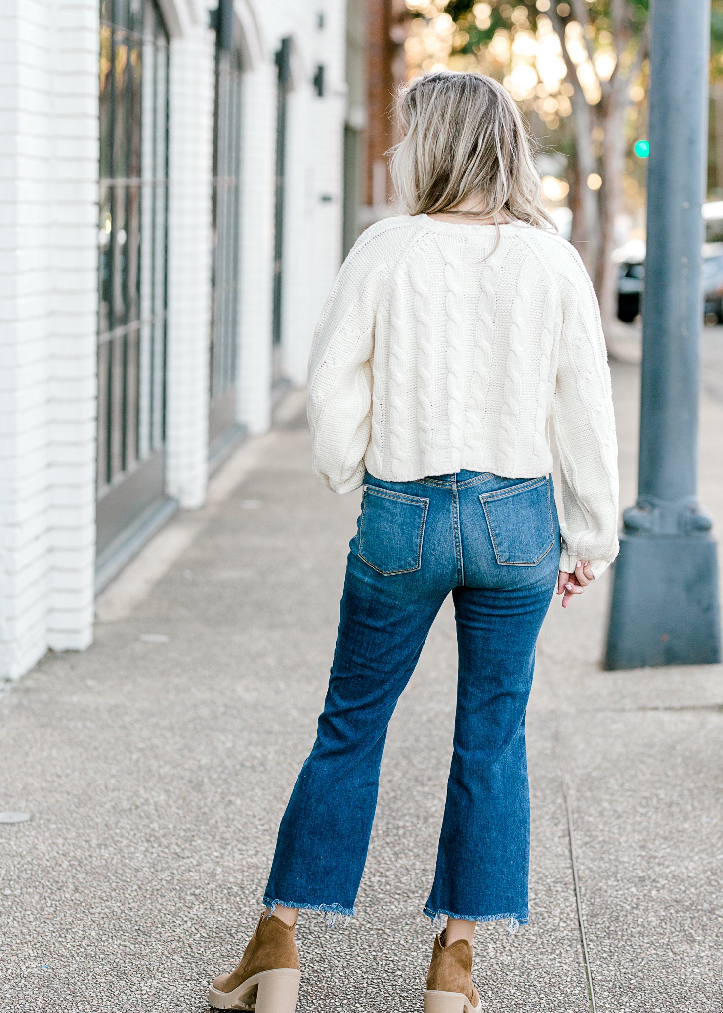 Back view of Blonde model wearing a cream cable knit sweater.