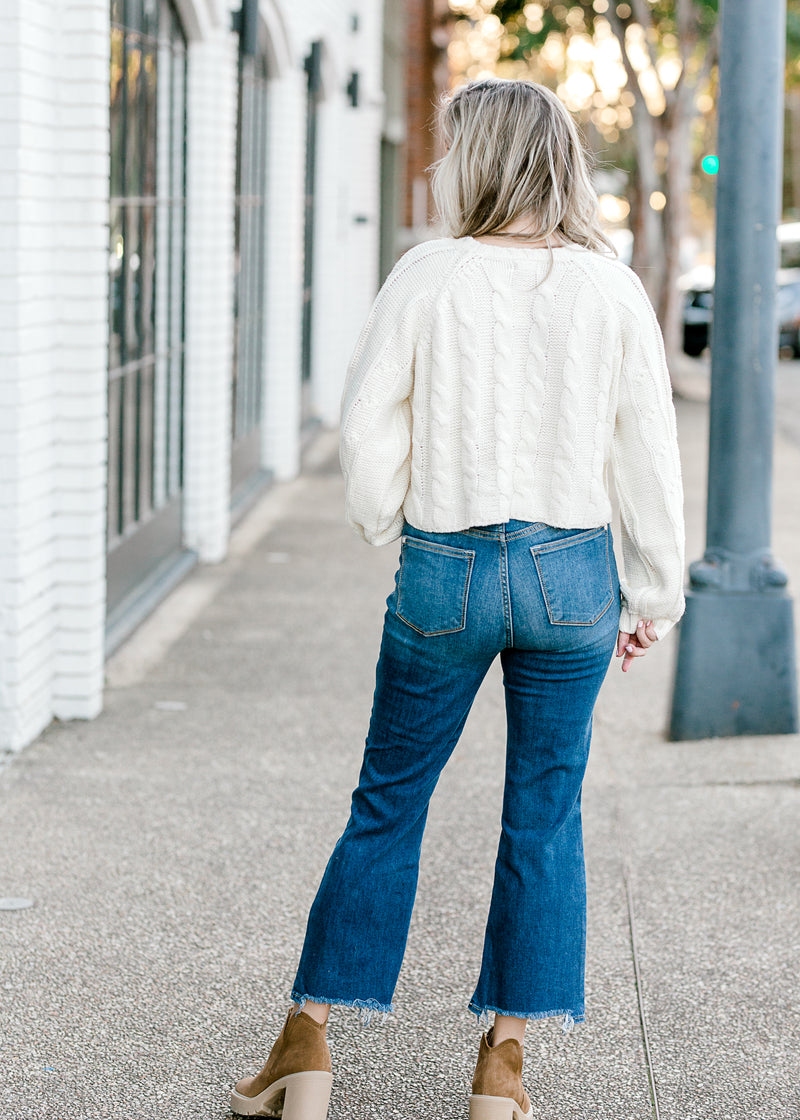 Back view of Blonde model wearing a cream cable knit sweater.