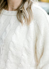 Close up of blonde model wearing a cream cable knit sweater.