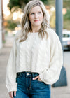 Blonde model wearing a cream cable knit sweater.