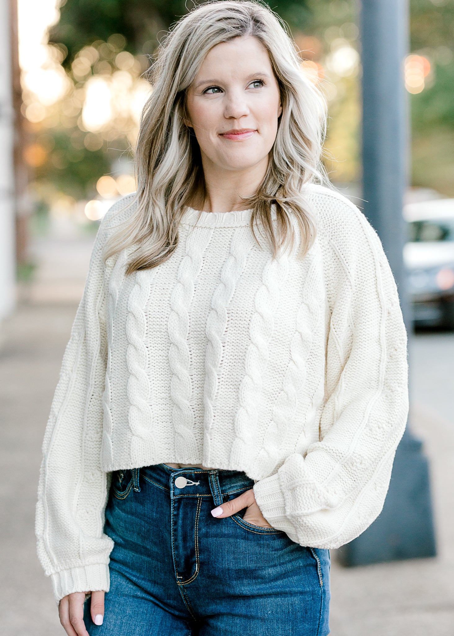 Blonde model wearing a cream cable knit sweater.