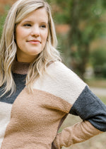 Close up view of Blonde model wearing cream, camel, gray and brown color block sweater.