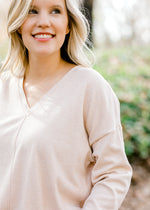 Close up view of Blonde model wearing a cream v-neck sweater.
