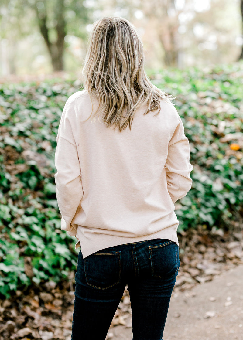 Back view of Blonde model wearing a cream v-neck sweater.