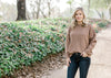 Blonde model wearing light brown sweater with exposed seam.