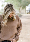 Close up view of Blonde model wearing light brown sweater. 