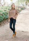 Blonde model wearing light brown sweater with jeans and booties. 