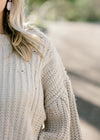 Close up view of Blonde model warning a cream sweater with bubble long sleeves. 