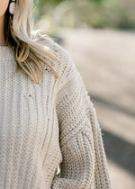 Close up view of Blonde model warning a cream sweater with bubble long sleeves. 