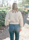 Back view of Blonde model warning a cream sweater with bubble long sleeves. 