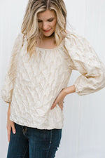 Blonde model wearing a textured cream blouse. 