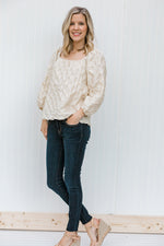 Blonde model wearing a textured cream blouse with jeans and heels.