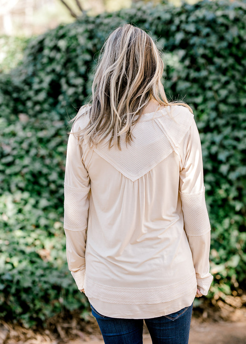 Back view of Blonde model wearing cream top with military details and mixed fabrics.