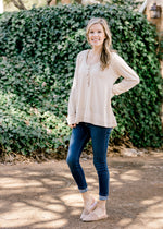 Blonde model wearing cream top with military details and mixed fabrics, jeans and slides.