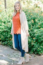 Blonde model wearing cream duster cardigan with coral top, jeans and boots. 