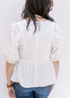 Back view of model wearing a white babydoll top with a zipper in back and bubble sleeves. 