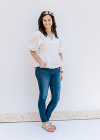 Model wearing jeans and sandals with a white babydoll top with a v-neck and bubble short sleeves. 