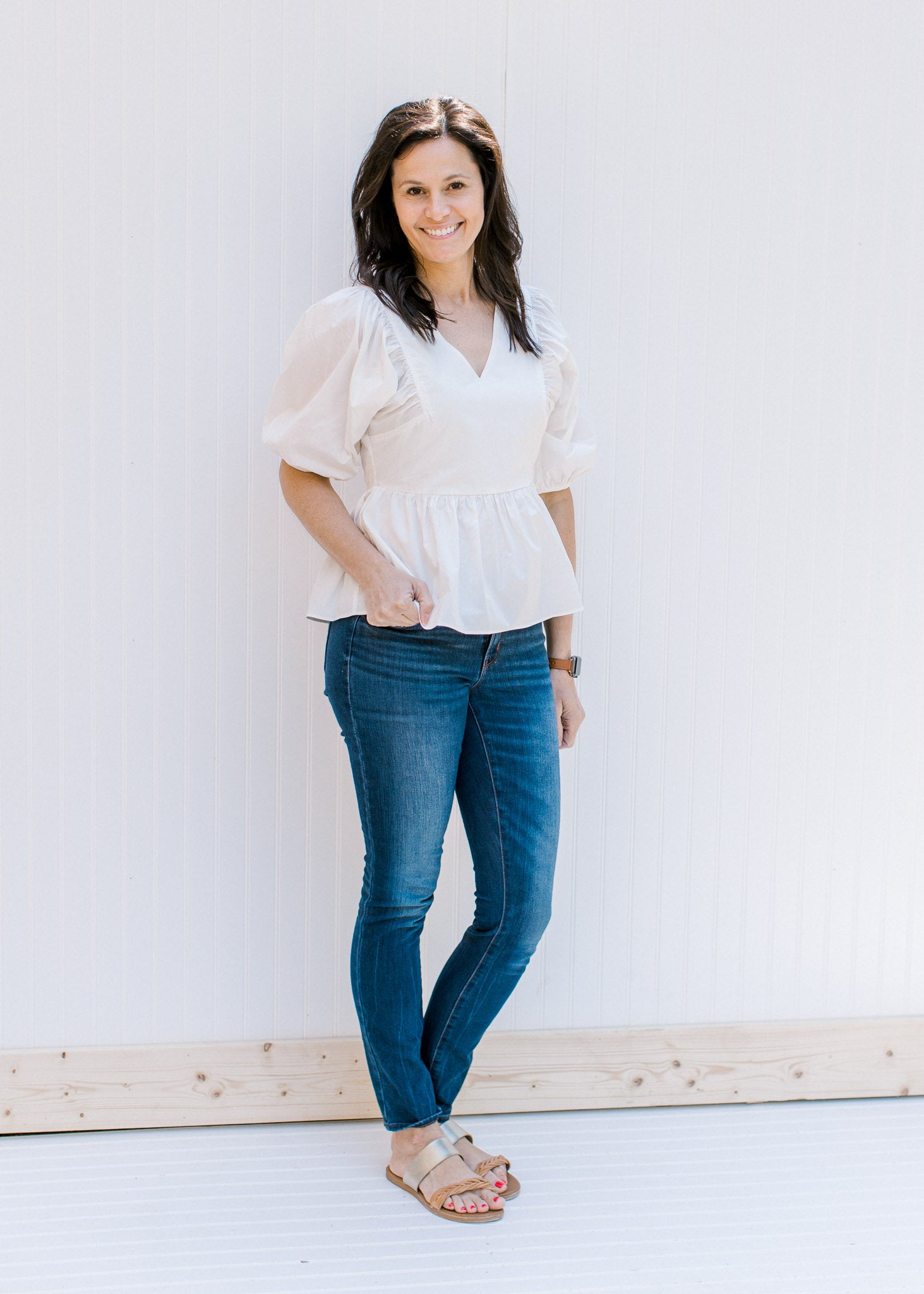 Model wearing jeans and sandals with a white babydoll top with a v-neck and bubble short sleeves. 