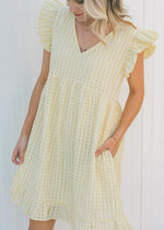Model wearing a yellow short sleeve, checkered dress with ruffle capped sleeves. 
